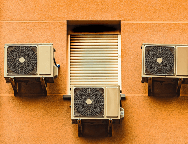 Three Air conditioning units attached to an orange wall